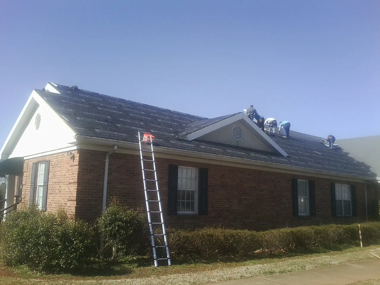 Crew tearing shingles off a brick ranch roof with a ladder set — Metal Roof Repair work by our crew in Nineveh