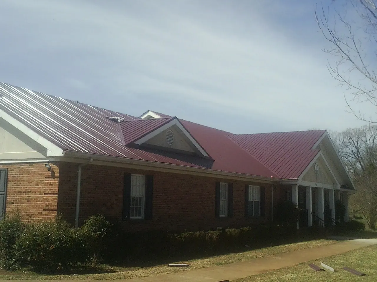 Red metal roof with gabled entries on a long brick building, from a Hail Damage Roof Repair job in Nineveh