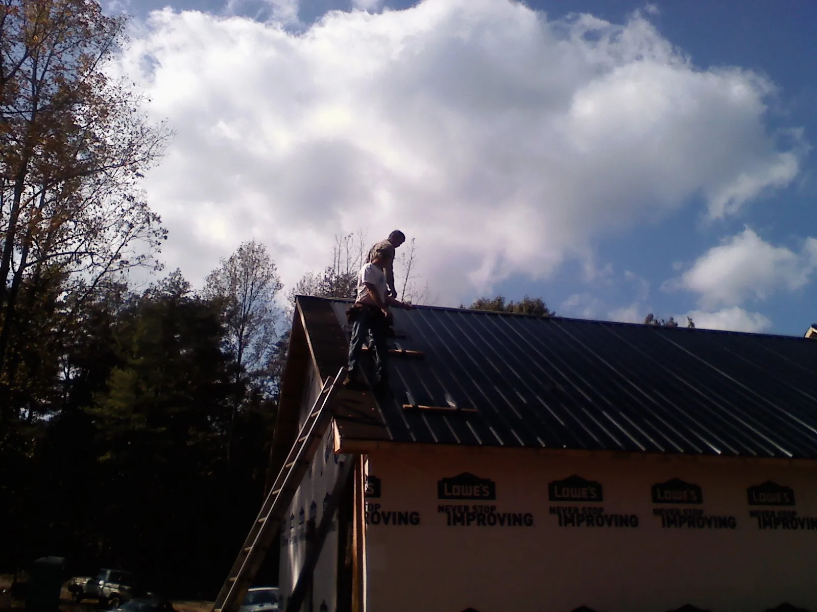 Roofer fastening dark metal panels high against a cloudy sky, from a Roof Inspection job in Nineveh